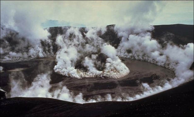 The crater of Galunggung volcano steams on February 5, 1983, a month after the end of the 1982-83 eruption. Vigorous steam clouds issue from a late-stage cinder cone formed in the center of the crater and from the margins of the interior crater wall. A lake that had begun forming in the crater at the time of this photo eventually grew to entirely cover the cinder cone. (© Don Peterson, 1983, USGS)